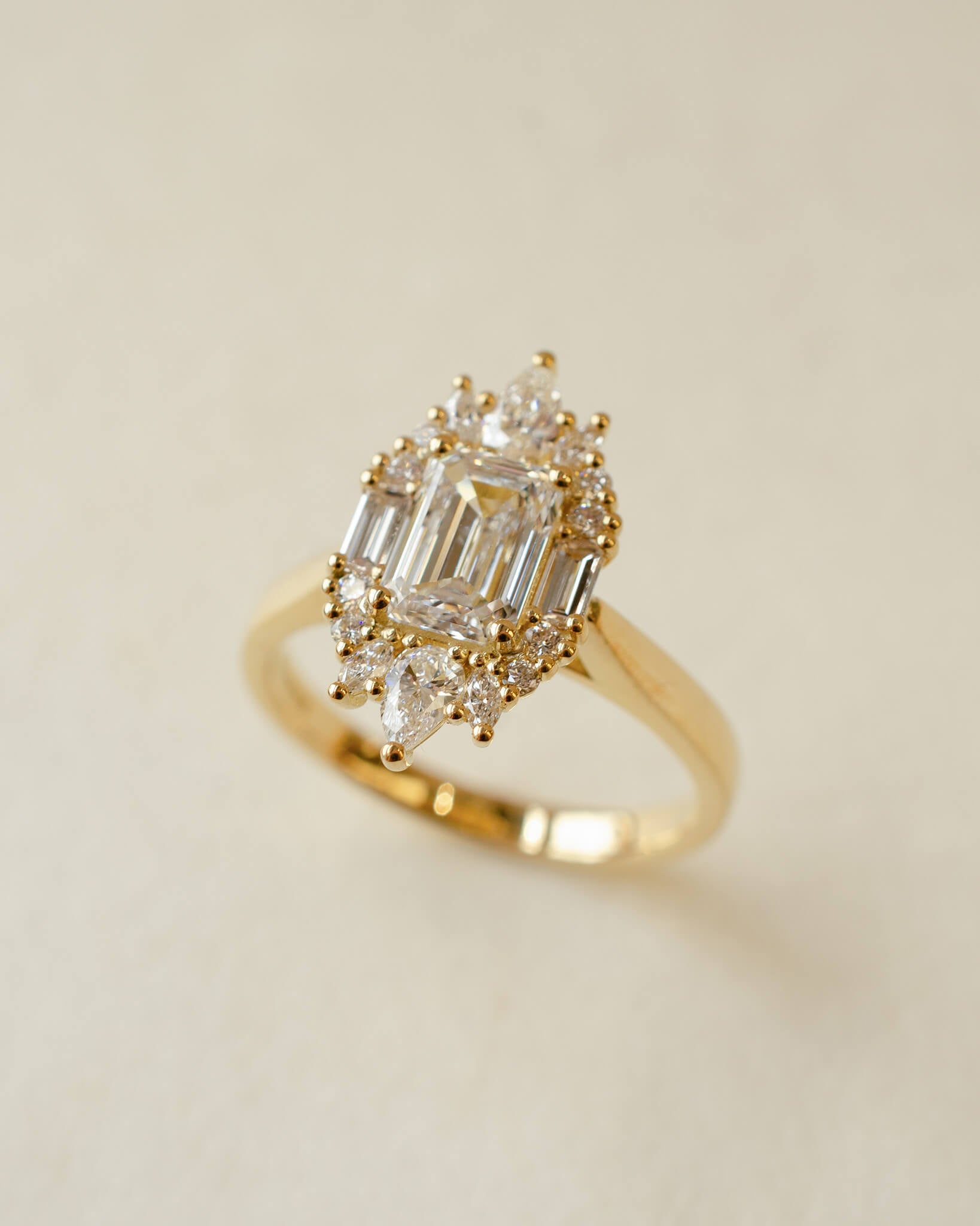 Gold ring with emerald-cut and pear-shaped diamonds on a beige background