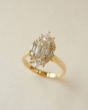 Gold ring with emerald-cut and pear-shaped diamonds on a beige background